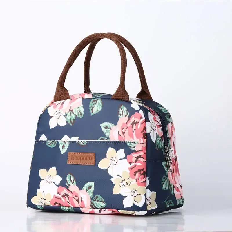 sac isotherme repas bleu marine à motifs floraux roses et blancs, vu de face sur fond blanc, avec poignées marron et texture imperméable brillante
