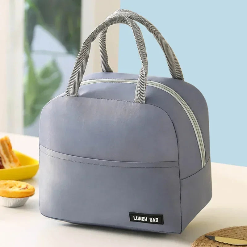 Vue de face d’un sac isotherme repas  gris avec poignées grises, posé sur une table de cuisine éclairée, idéal pour transporter un déjeuner au bureau ou en pique-nique.
