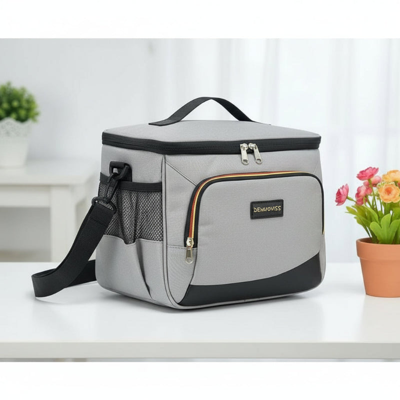 Sac isotherme repas gris de profil posé sur une table, avec bandoulière et un pot de fleurs colorées placé à droite.