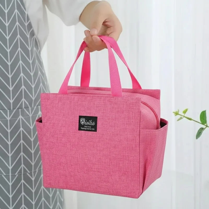 Sac isotherme rose porté à la main, avec anses et poches latérales, utilisé pour transporter un repas