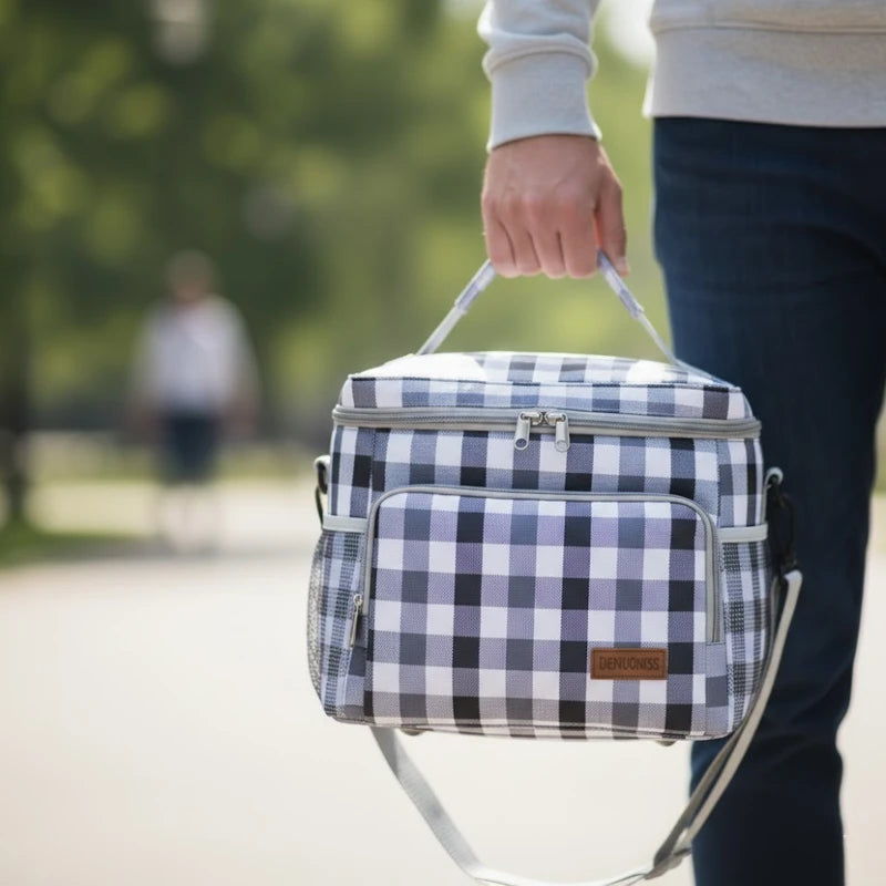 Sac isotherme motif vichy vert porté à la main par une personne en extérieur, avec fond de parc flou
