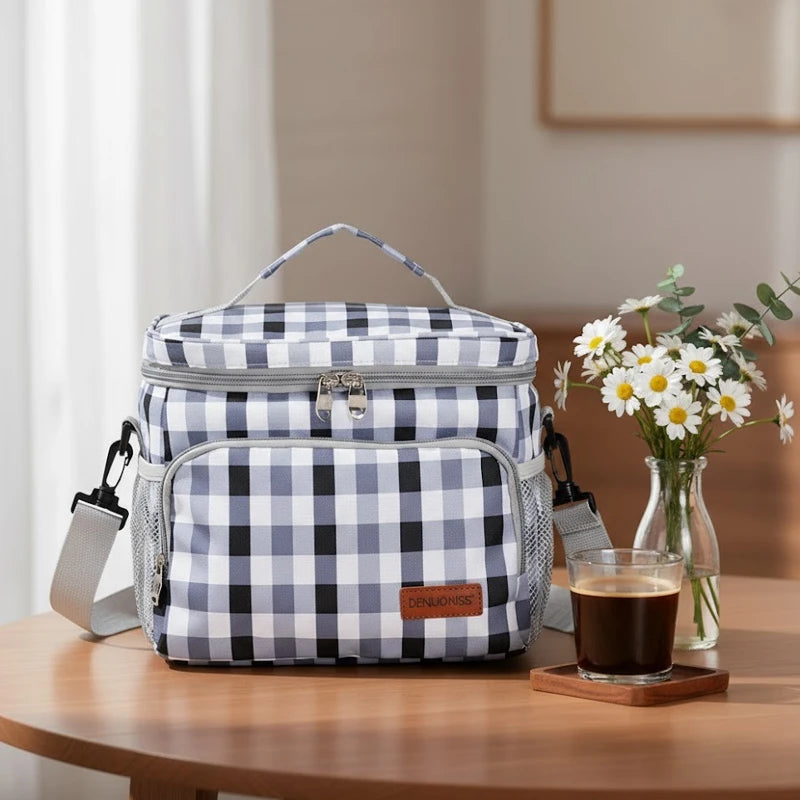 Sac isotherme motif vichy vert posé sur une table ronde avec un petit bouquet de fleurs et un verre de café