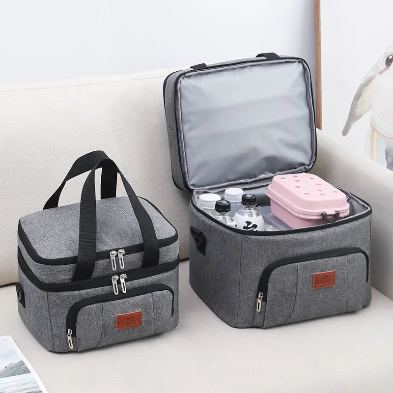 Deux sacs repas isothermes gris à double compartiment, l’un fermé et l’autre ouvert avec bouteilles et boîte repas à l’intérieur.