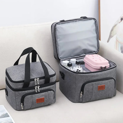 Deux sacs repas isothermes gris à double compartiment, l’un fermé et l’autre ouvert avec bouteilles et boîte repas à l’intérieur.