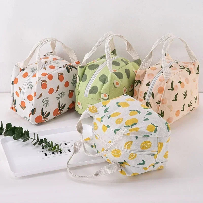 Quatre sacs isothermes en tissu avec des motifs colorés de fruits et de feuilles citrons, avocats, oranges et pêches disposés sur une table blanche dans un décor lumineux.