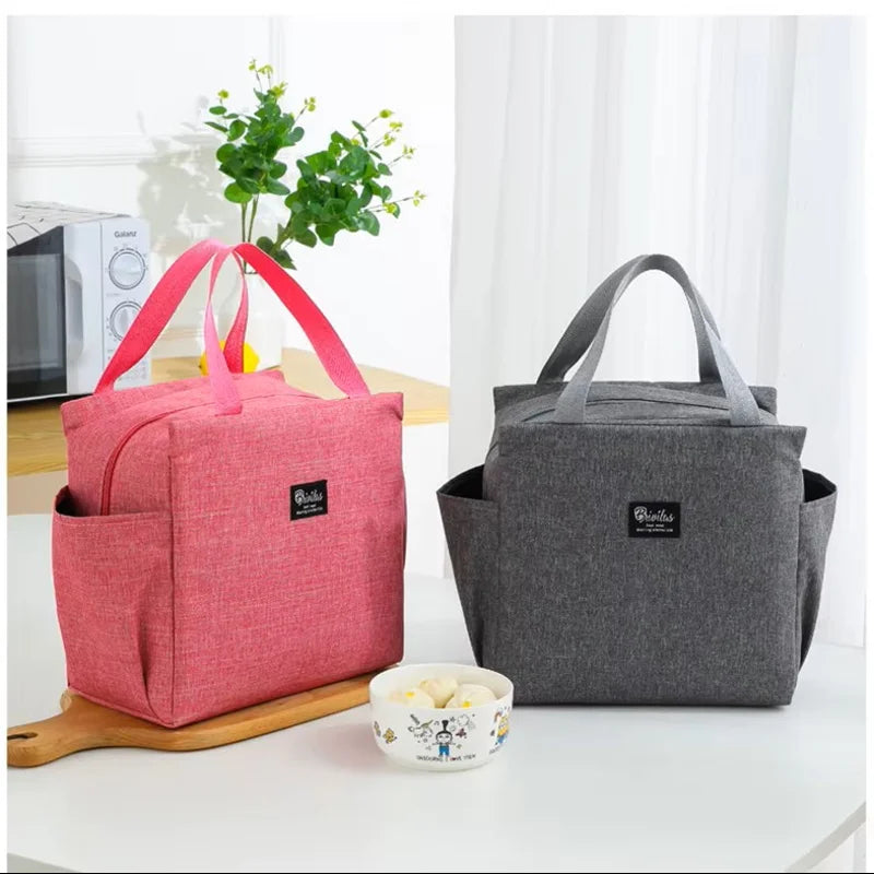 Deux sacs isothermes posés sur une table, un rose et un gris, présentés côte à côte avec un bol et une plante en arrière-plan