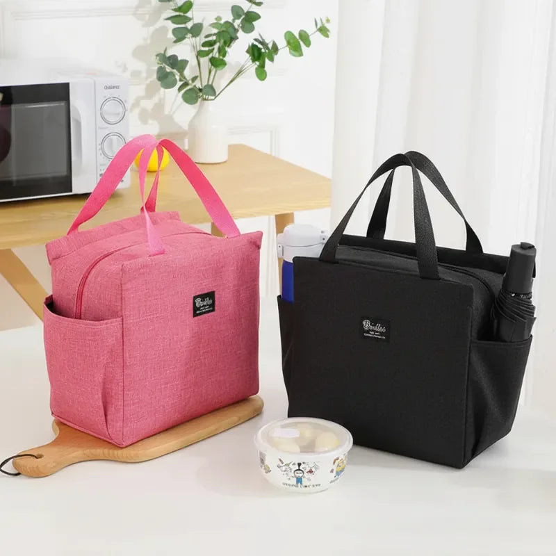 Deux sacs isothermes posés sur un bureau, un rose et un noir, utilisés comme lunch bag avec bol repas